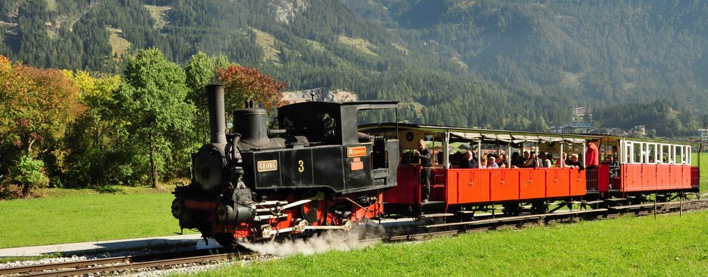 Die schwarze Achenseebahn auf den Gleisen vor Bergkulisse.