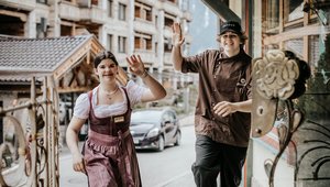 Zwei Kraftplatz-Lehrlinge winken beim Raufgehen der Eingangstreppe 